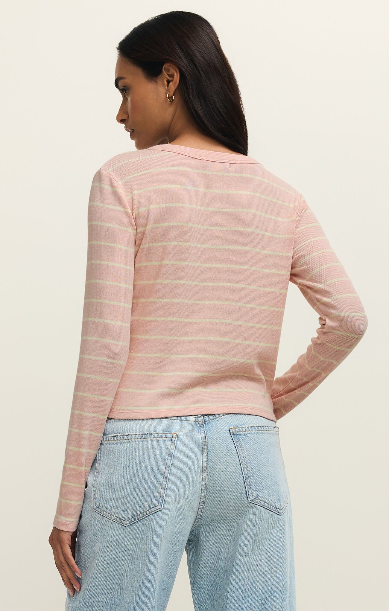 Woman wearing a pink striped long-sleeve top and light blue jeans on a beige background