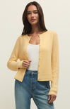 Woman wearing a yellow cardigan over a white top and blue jeans on a plain background