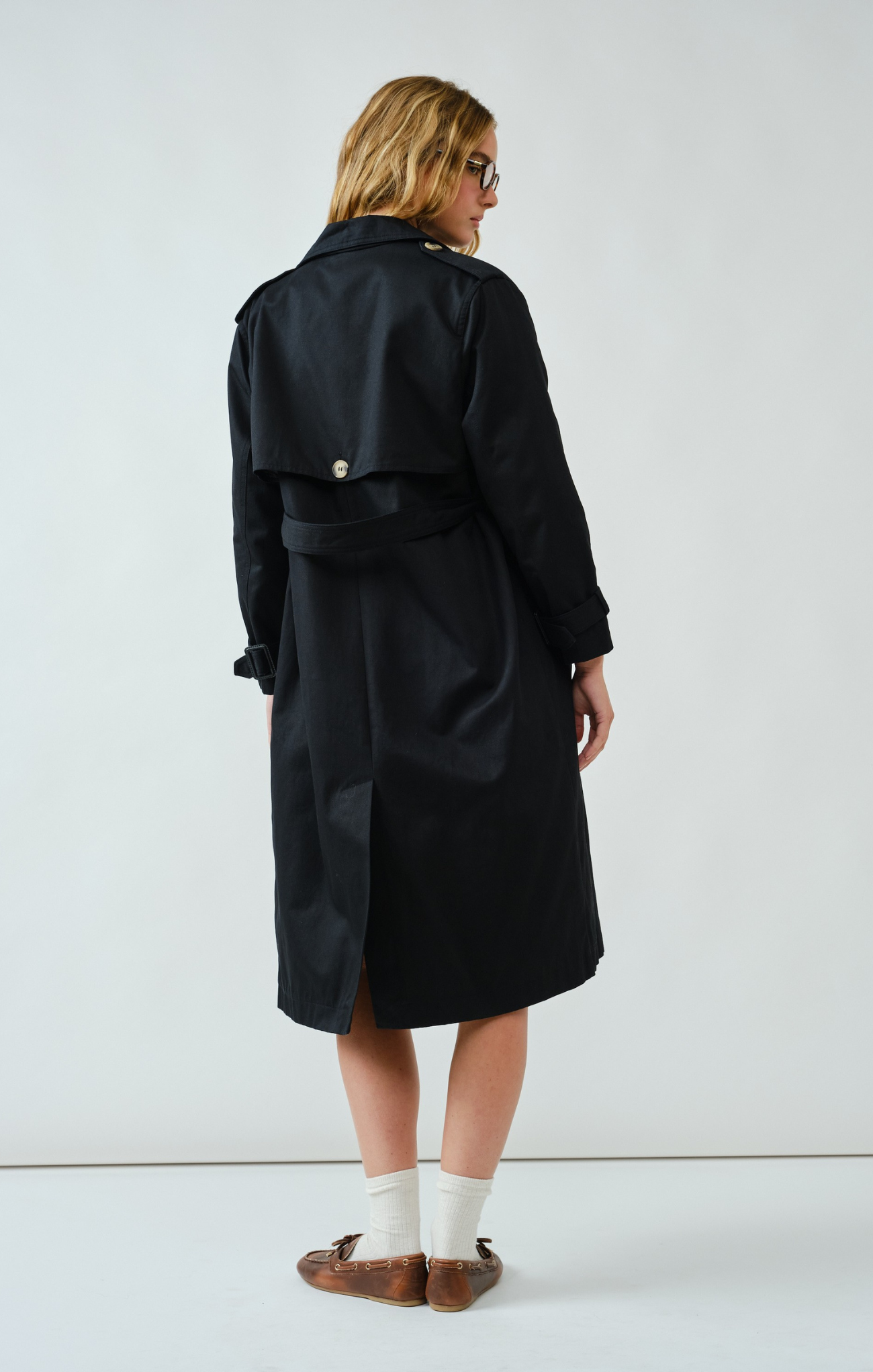 Person wearing a black trench coat on a white background