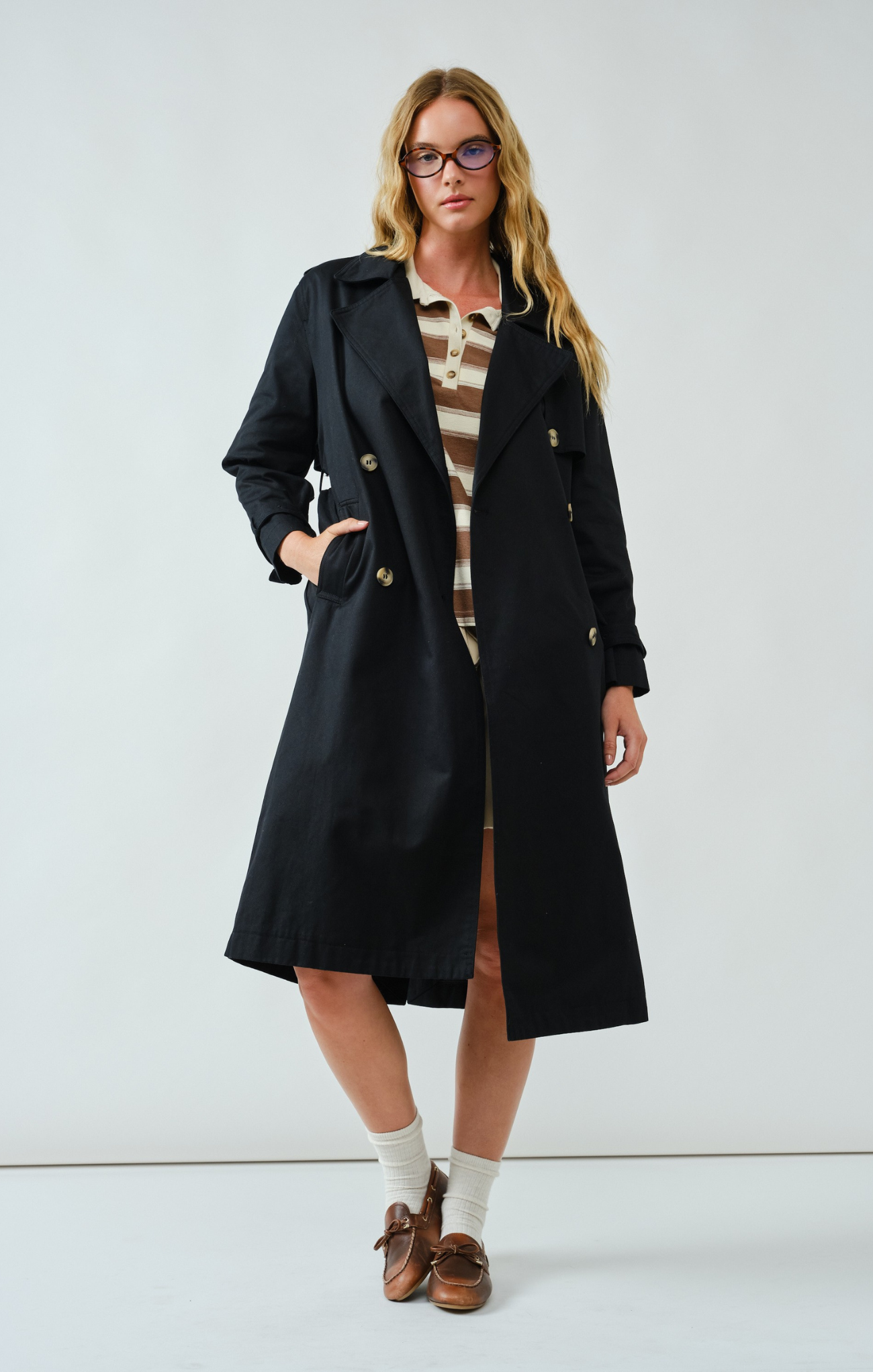 Woman wearing a black coat over a striped dress on a white background