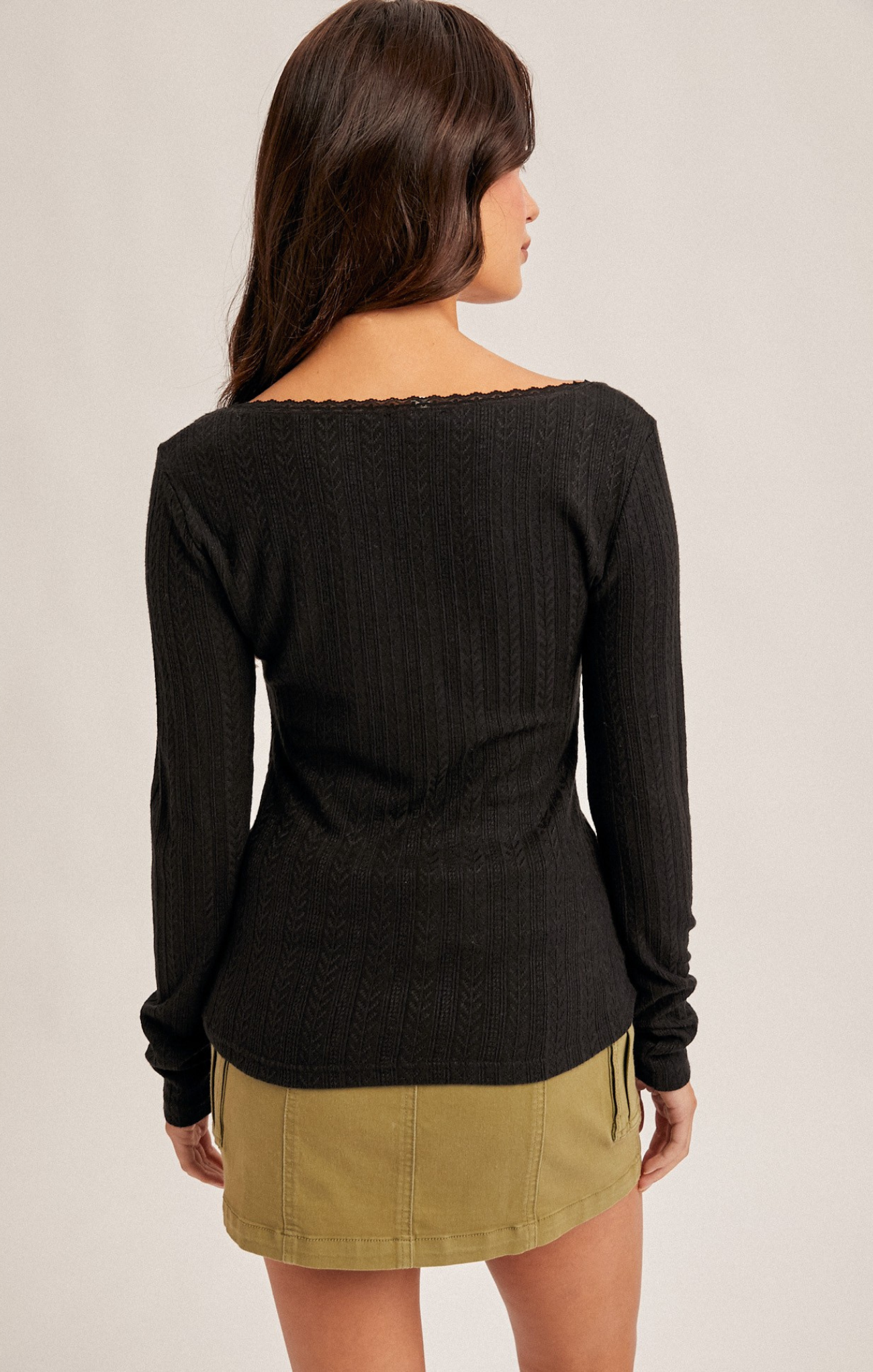 Woman wearing a black long-sleeve top and beige skirt on a plain background