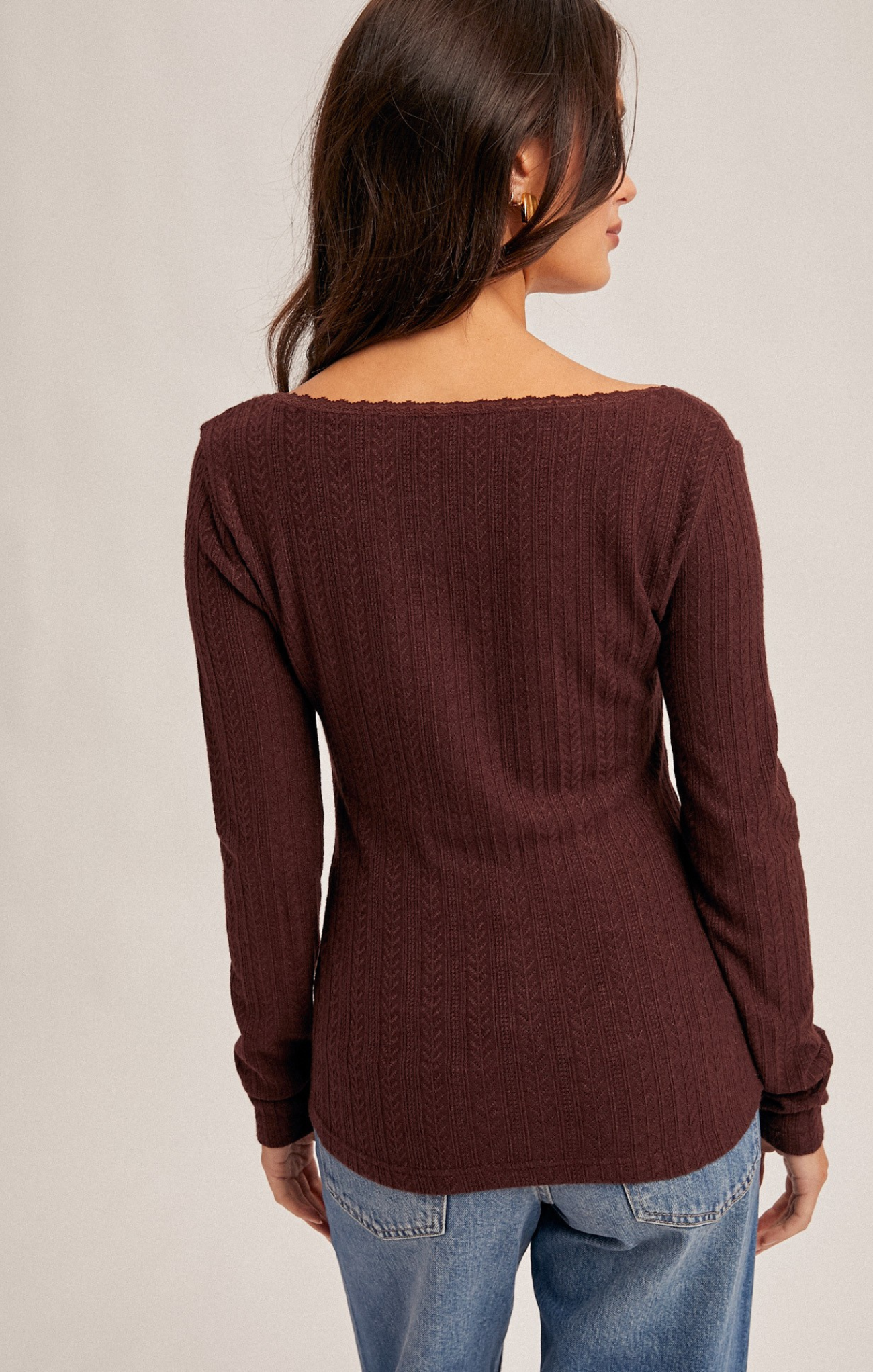 Woman wearing a brown ribbed sweater and blue jeans on a plain background