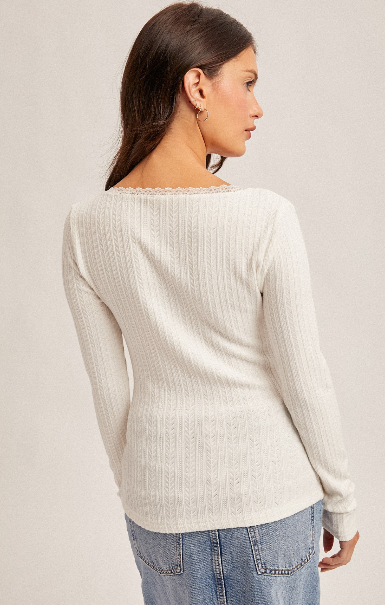 Woman wearing a white ribbed sweater and blue jeans on a plain background