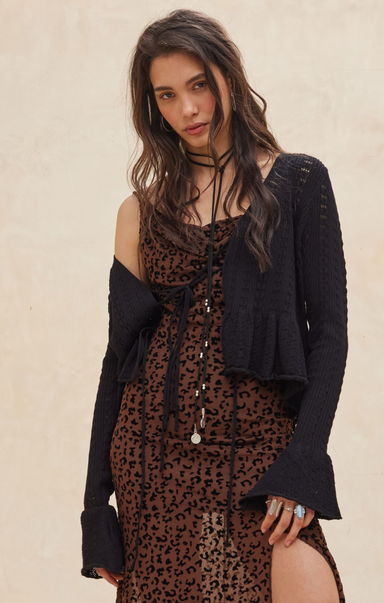 Woman wearing a leopard print dress with a black cardigan against a beige background