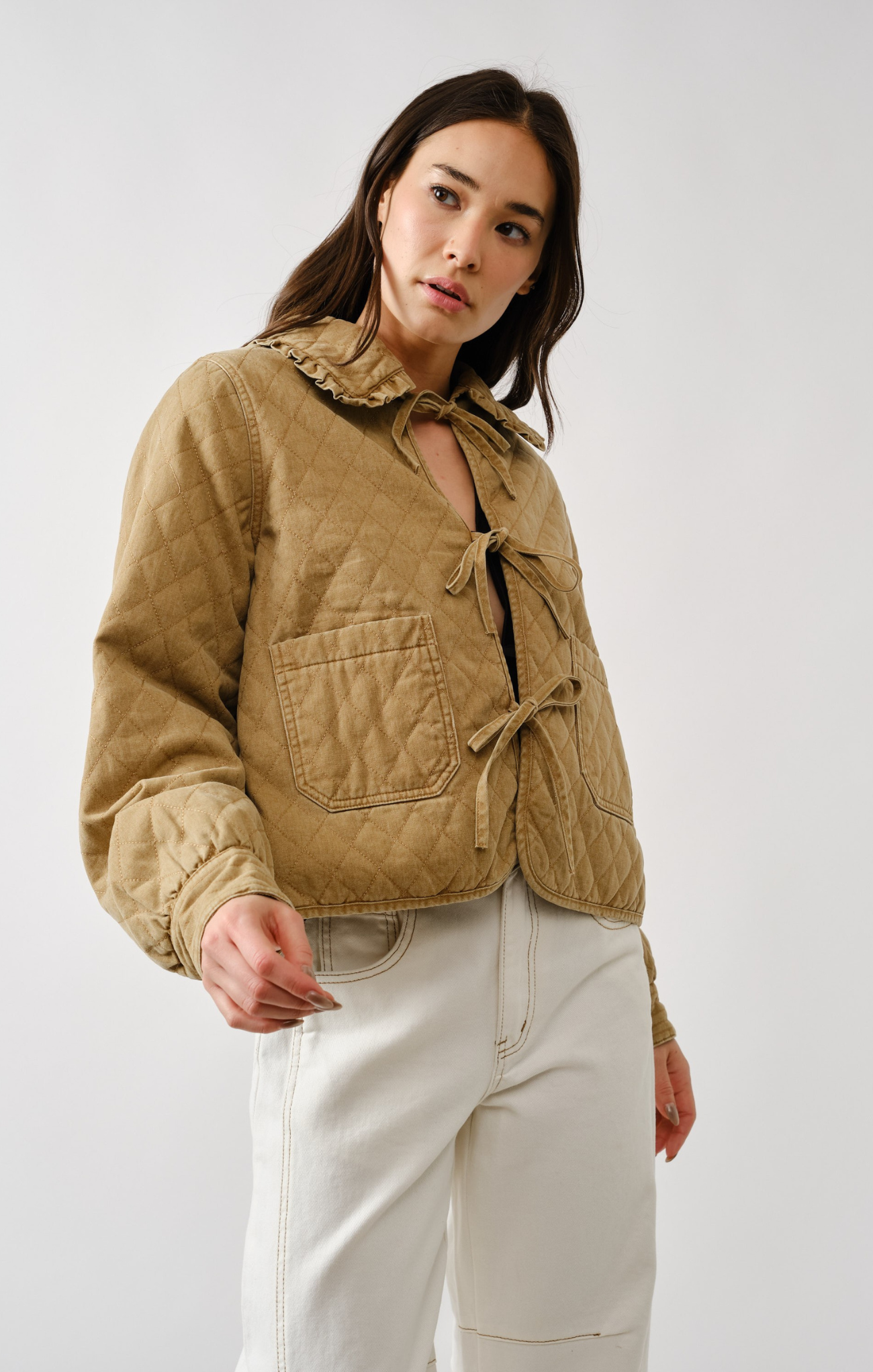 Woman wearing a beige quilted jacket and white pants against a plain background