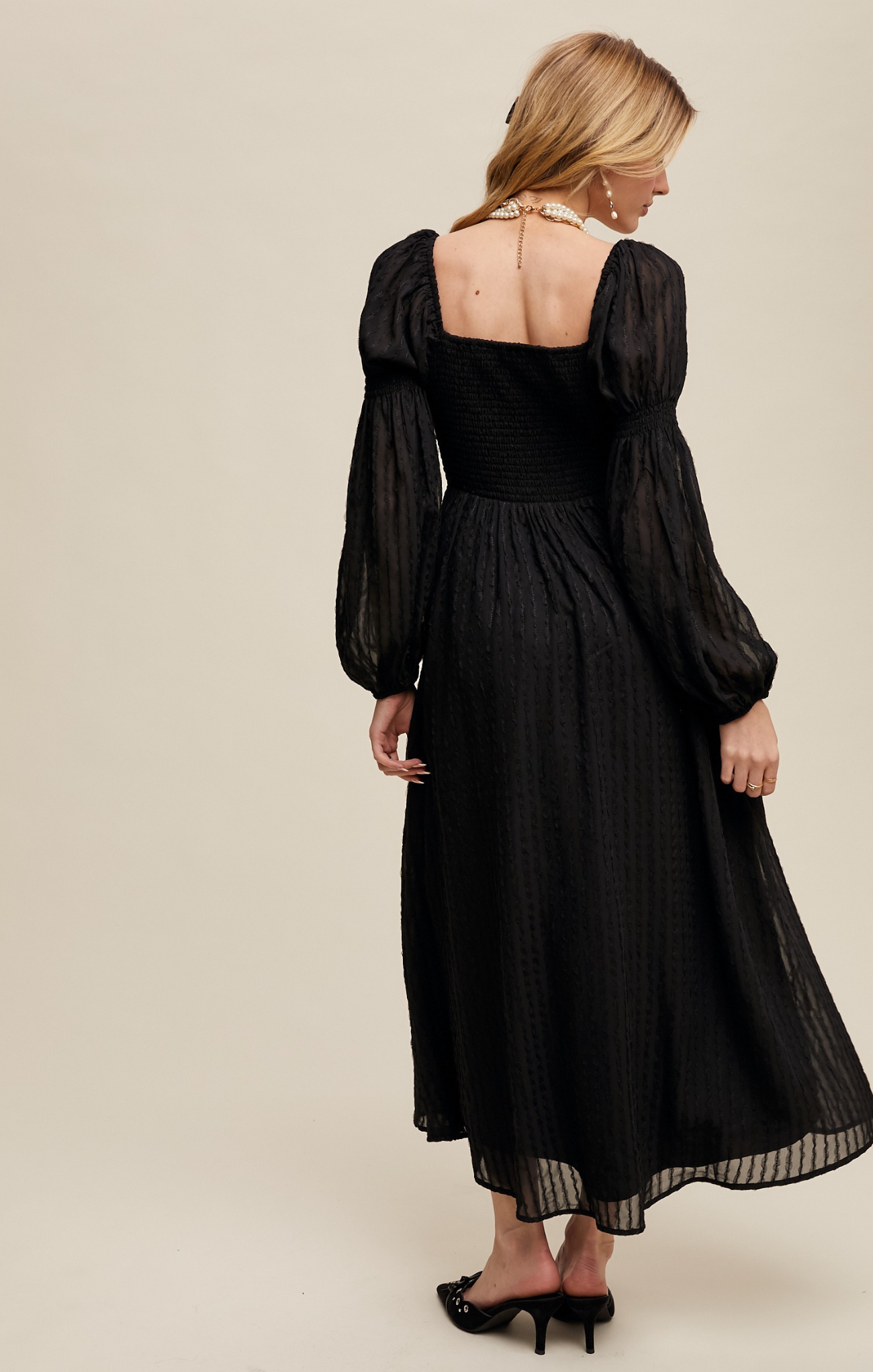 Woman wearing a black dress with sheer sleeves on a beige background