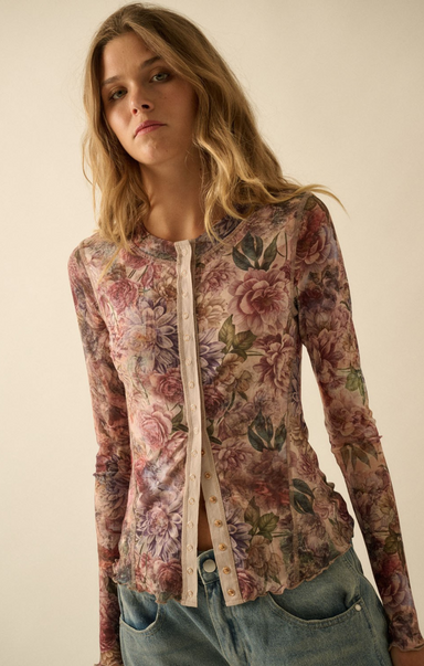 A woman wearing a long-sleeve floral button-front top with a cream placket, paired with blue jeans, photographed against a plain beige studio background.