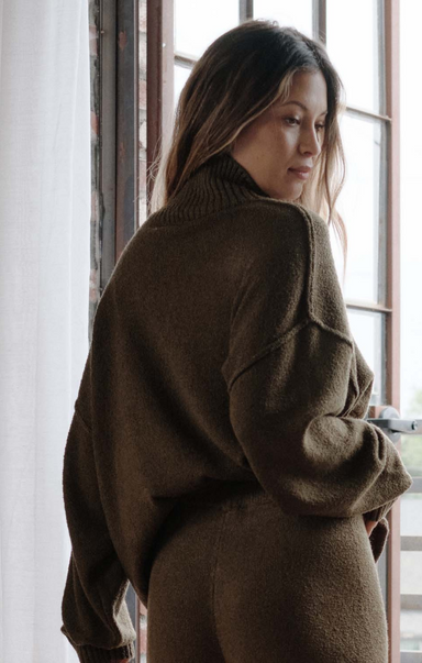 Woman wearing a brown sweater standing by a window