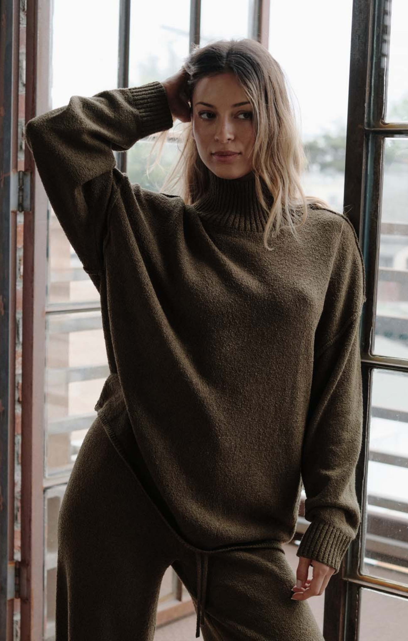 Woman wearing a green sweater and pants standing indoors.