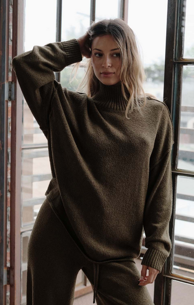 Woman wearing a green sweater and pants standing indoors.