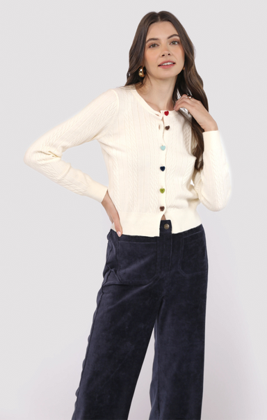 Woman wearing a cream cardigan and navy pants on a white background