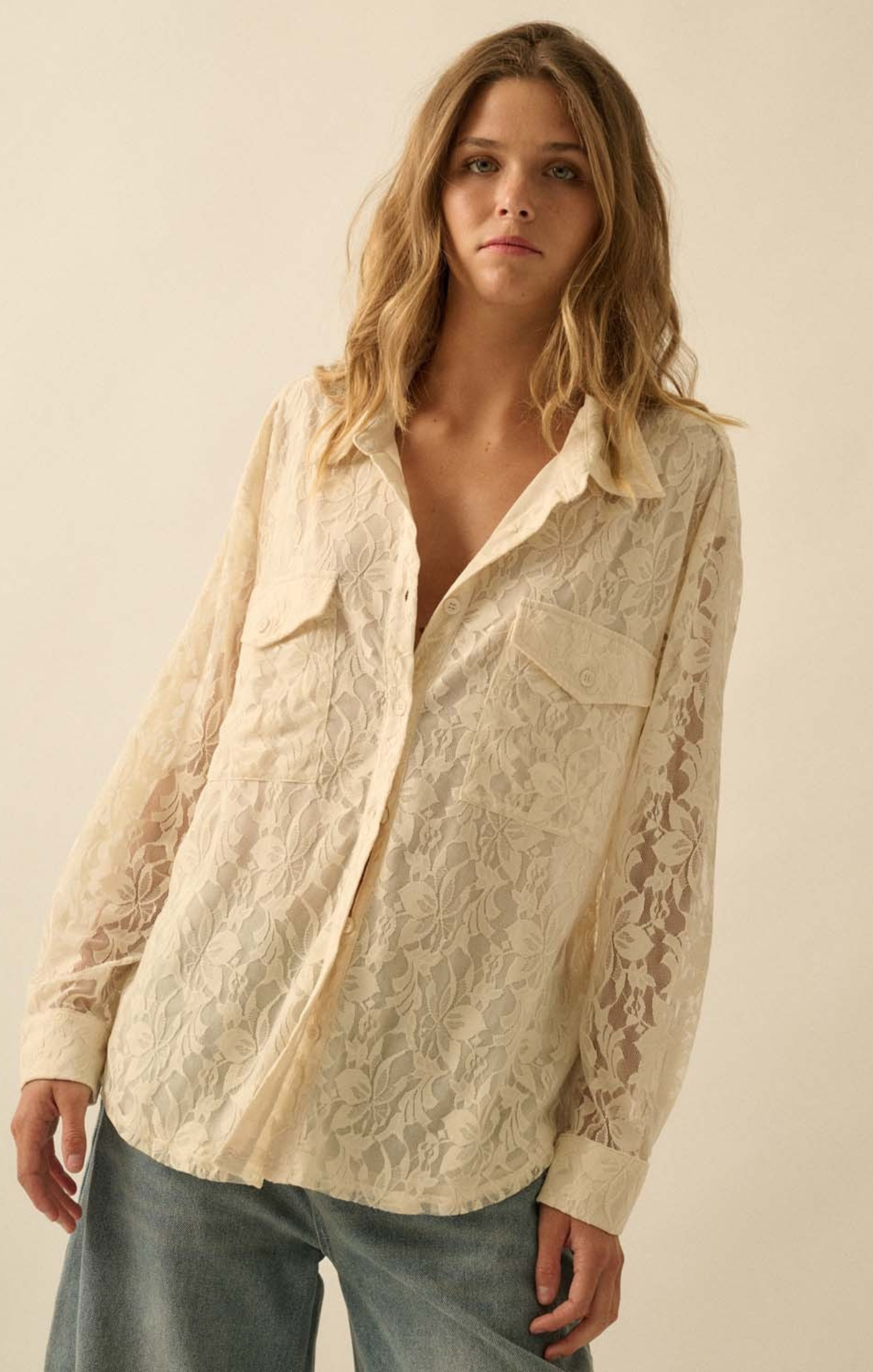 Woman wearing a beige lace shirt with a plain background