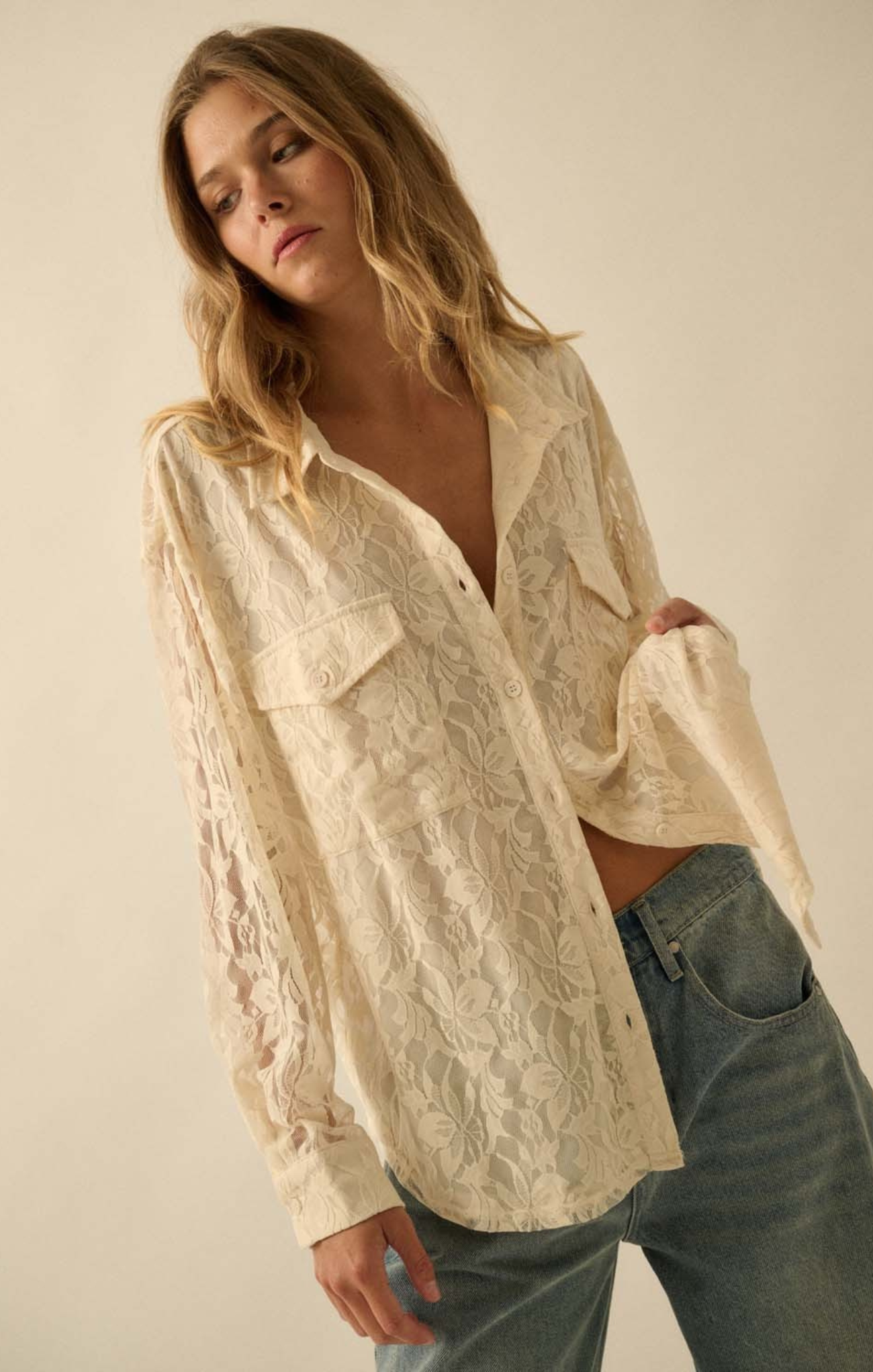 Woman wearing a lace blouse and jeans against a plain background