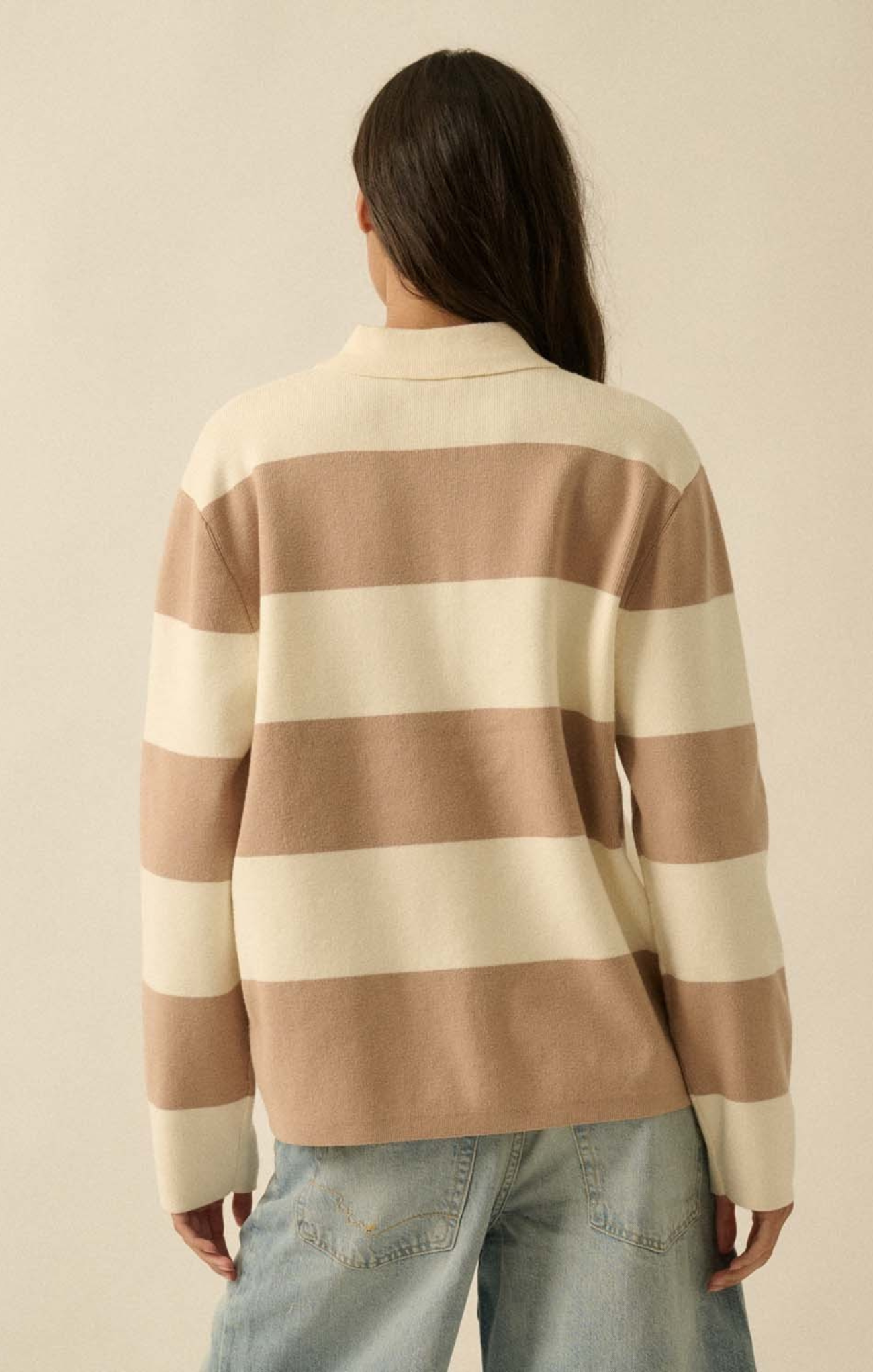 Person wearing a beige and brown striped sweater with light blue jeans on a beige background