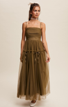 Woman wearing a long olive green dress with sheer overlay on a beige background