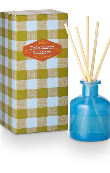 Blue diffuser bottle with wooden sticks next to a checkered box labeled 'Palo Santo Tobacco'.