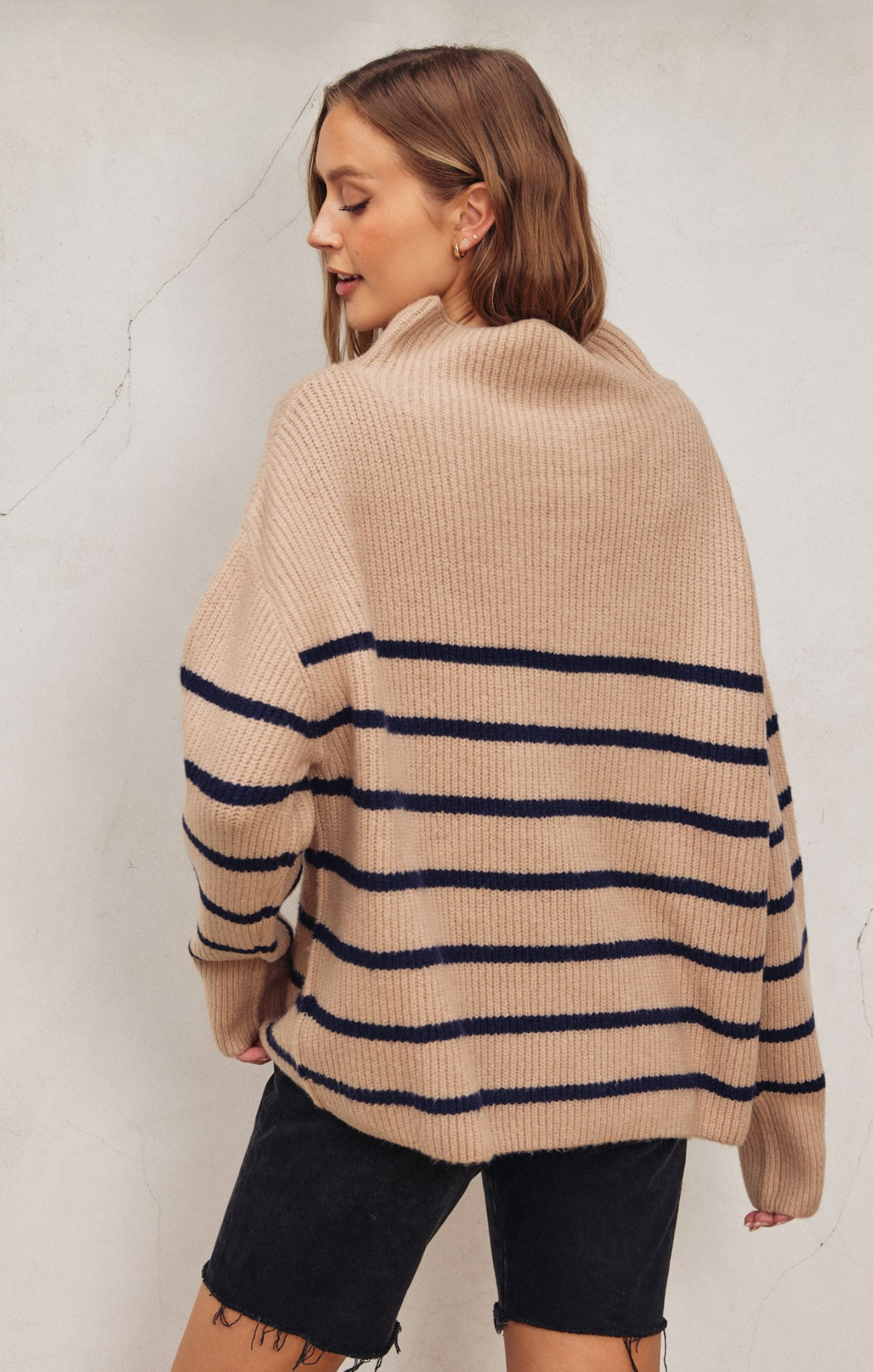 Woman wearing a beige sweater with navy stripes against a white background
