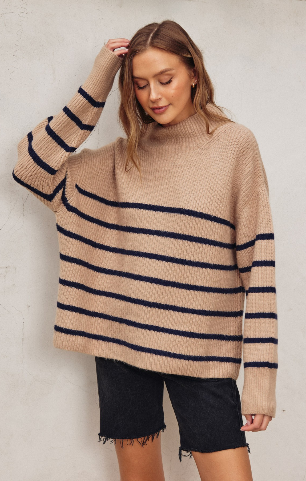 Woman wearing a beige sweater with navy stripes against a plain background