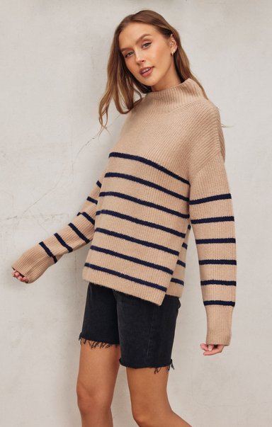 Woman wearing a beige sweater with navy stripes against a white background