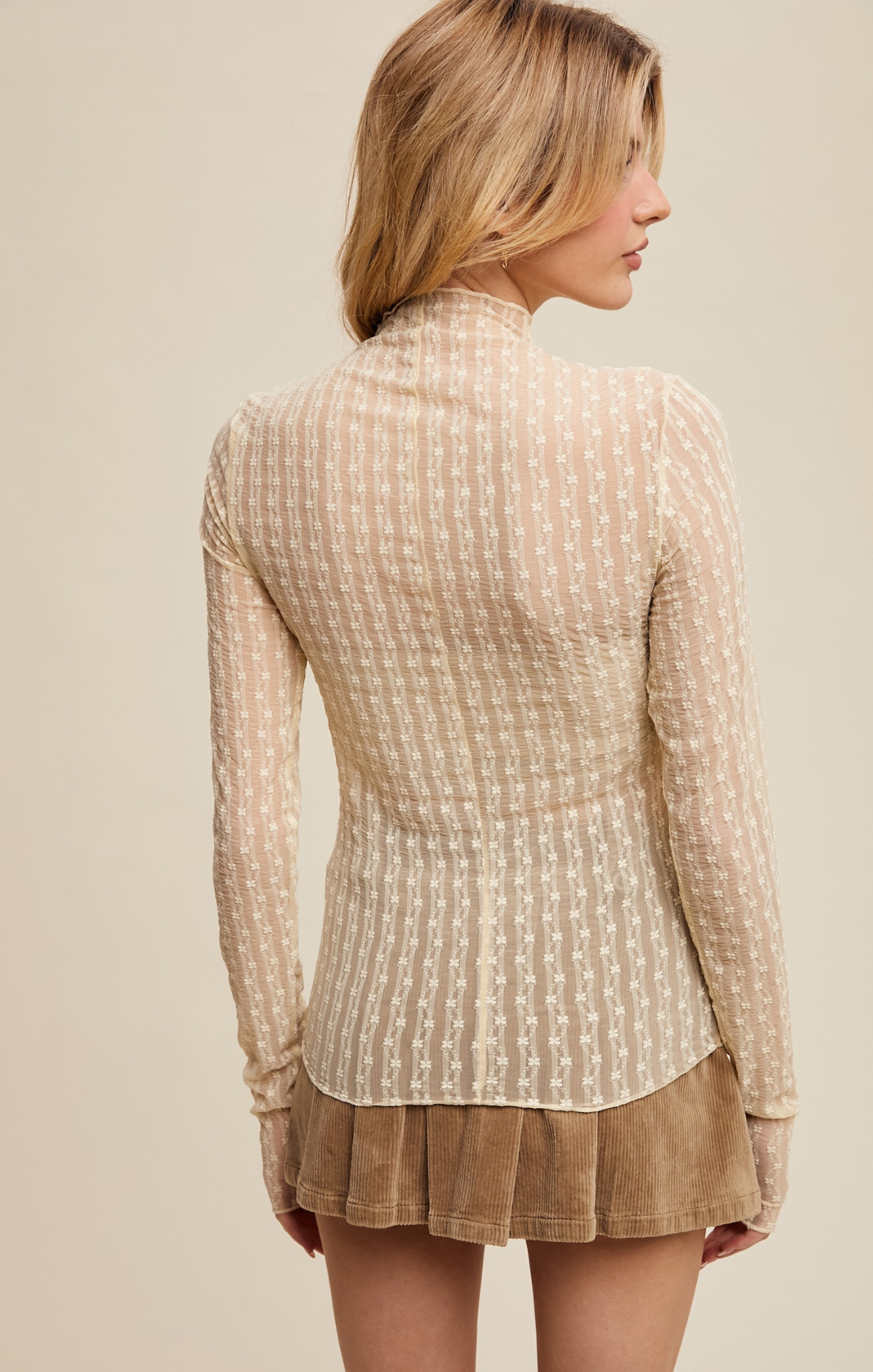 Woman wearing a beige patterned blouse and brown skirt on a beige background