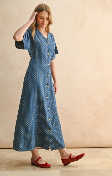 Woman wearing a blue dress with gold buttons against a beige background