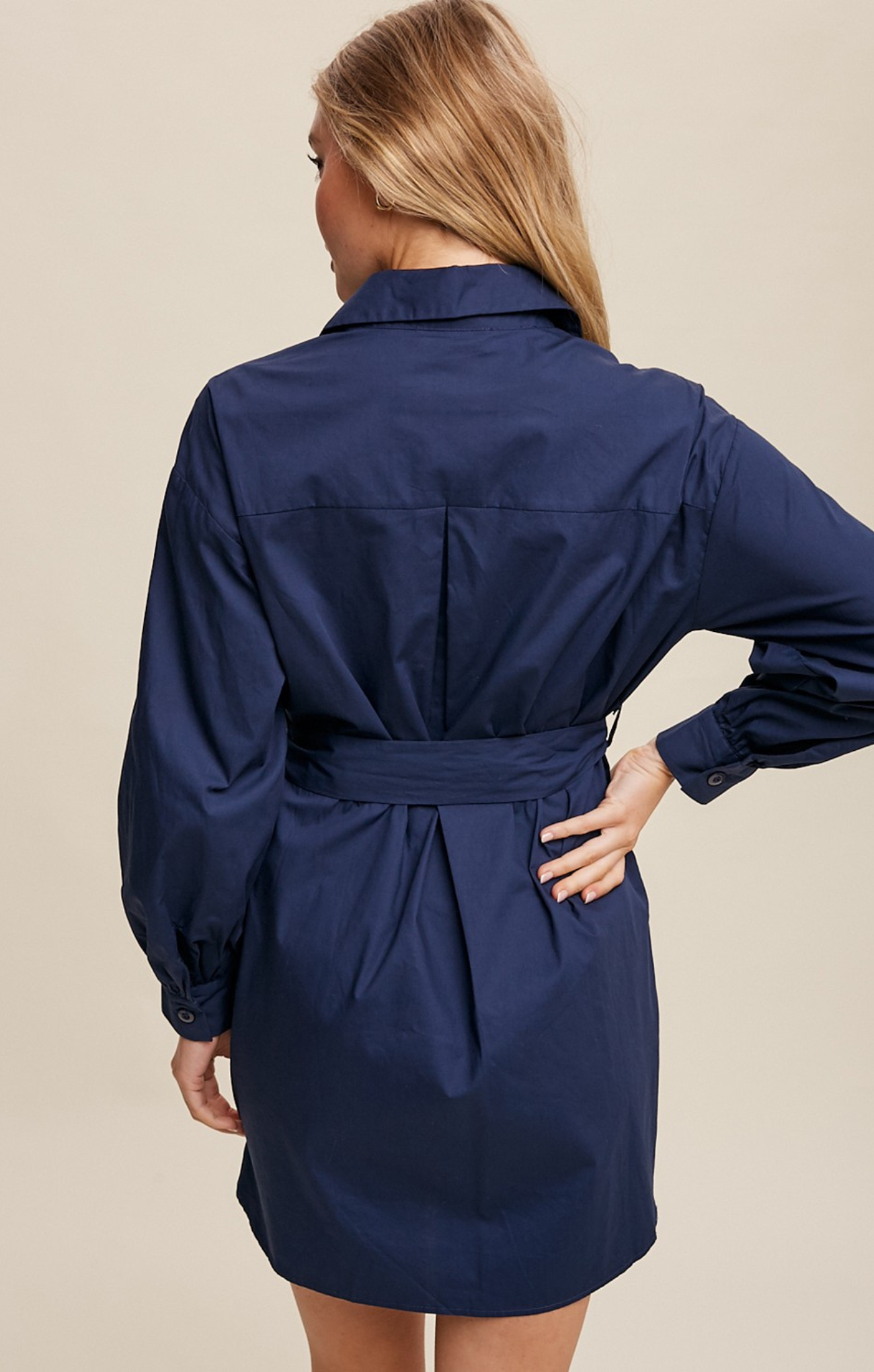 Woman wearing a navy blue dress with a belt against a beige background