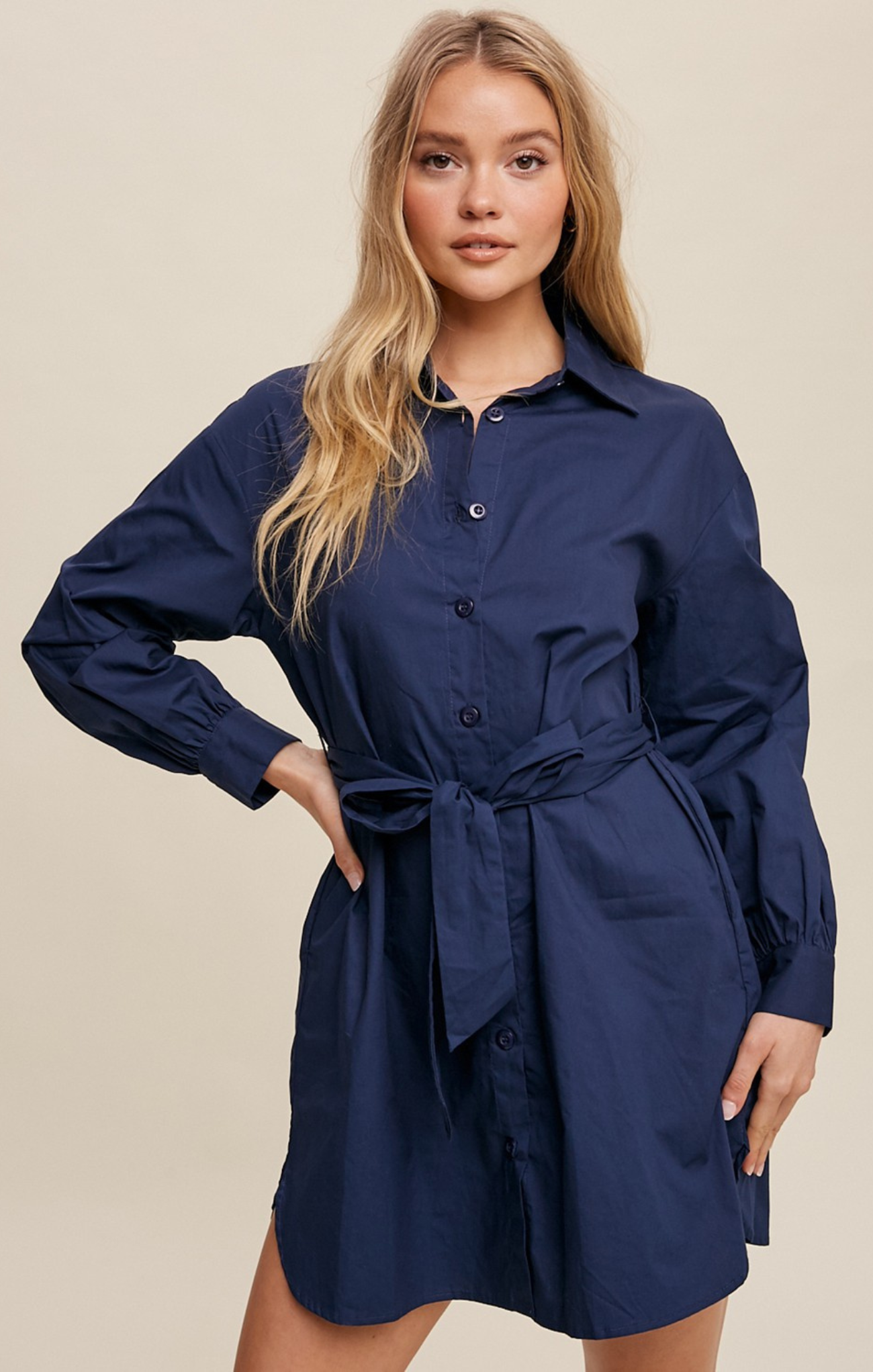 Woman wearing a navy blue dress with a belt against a beige background
