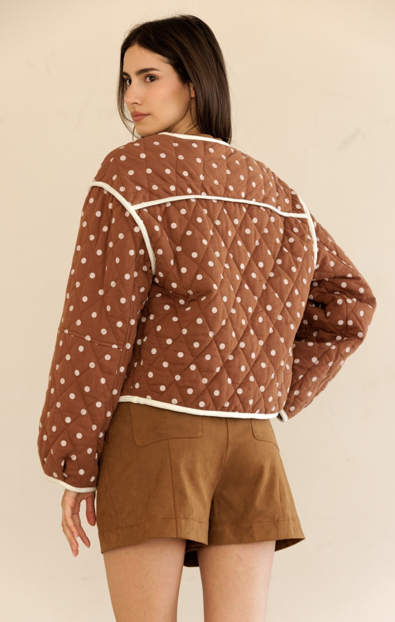 Woman wearing a brown quilted jacket with white polka dots and matching shorts on a beige background