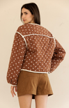 Woman wearing a brown quilted jacket with white polka dots and matching shorts on a beige background