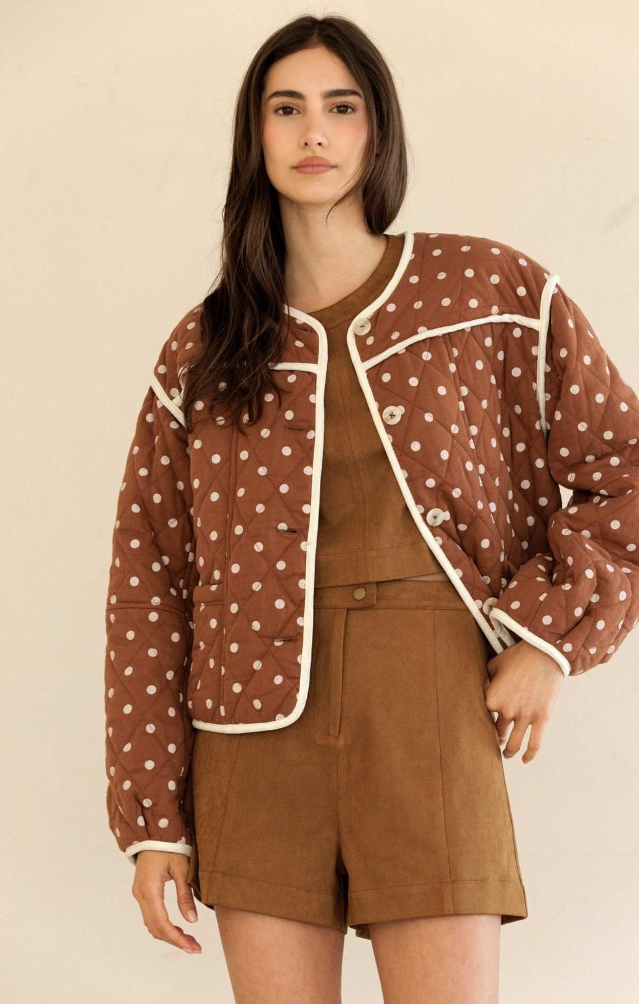 Woman wearing a brown polka dot jacket over a brown outfit on a beige background