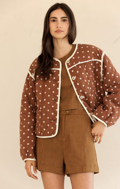 Woman wearing a brown polka dot jacket over a brown outfit on a beige background
