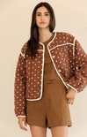 Woman wearing a brown polka dot jacket over a brown outfit on a beige background