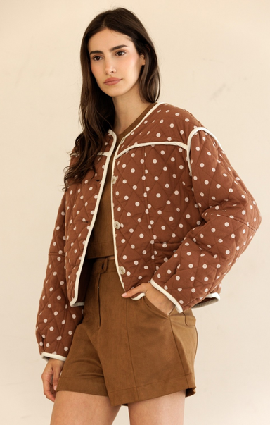 Woman wearing a brown polka dot jacket with a beige background