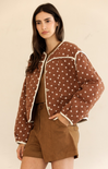Woman wearing a brown polka dot jacket with a beige background