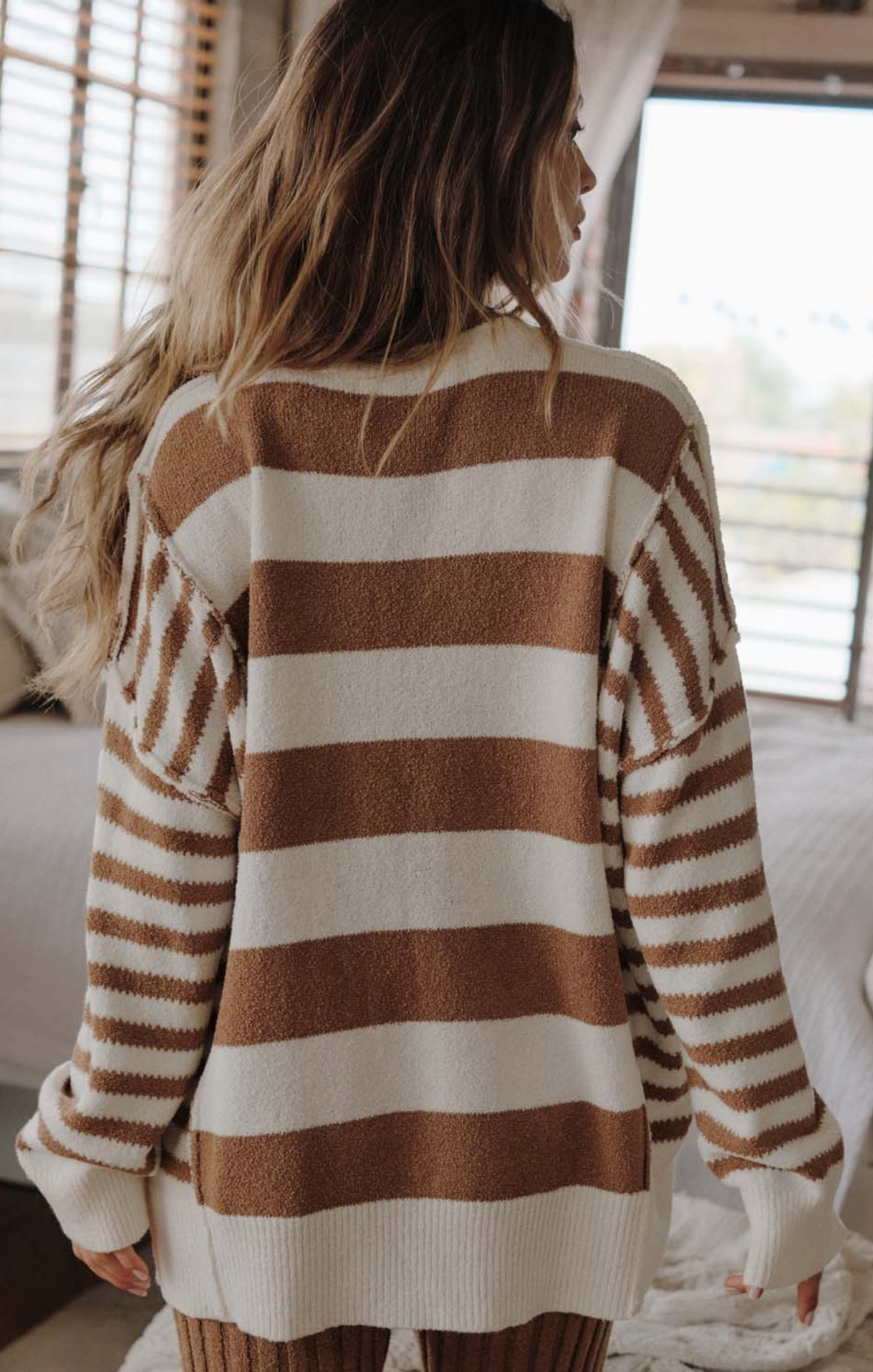 Person wearing a brown and white striped sweater in a cozy indoor setting.