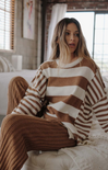 Woman wearing a brown and white striped sweater sitting on a couch.