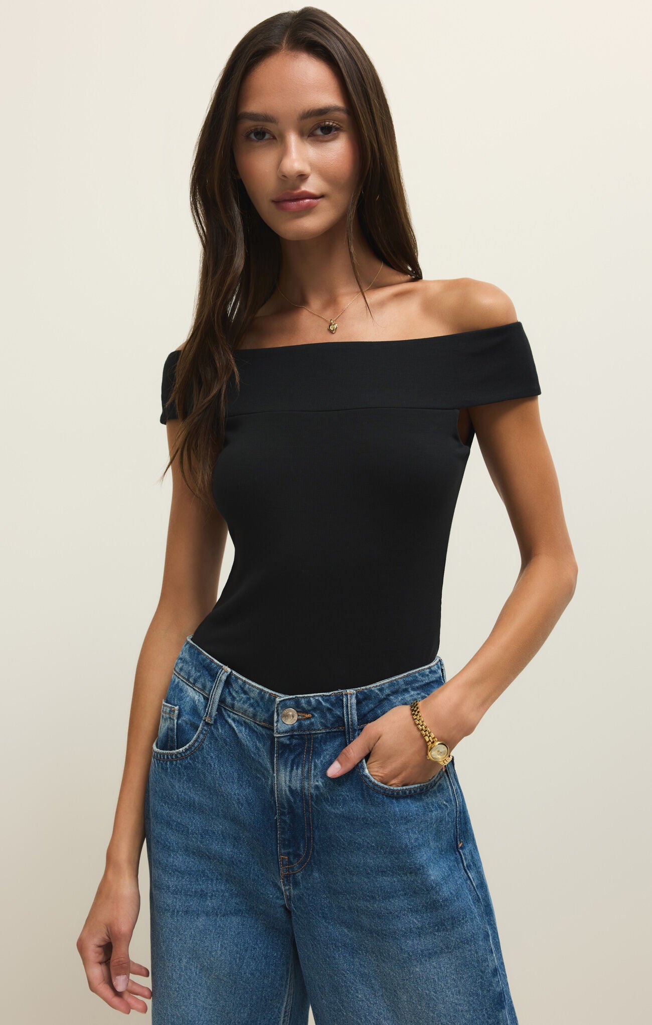 Woman wearing a black off-shoulder top and blue jeans against a plain background