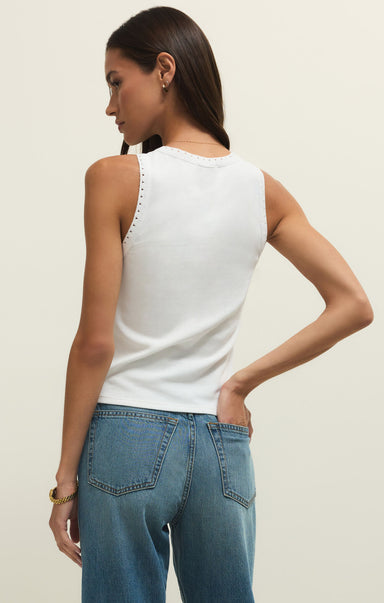 Woman wearing a white sleeveless top and blue jeans on a plain background