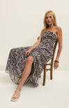 Woman wearing a floral one-shoulder dress sitting on a chair against a white background