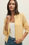 Woman wearing a yellow cardigan over a white top and blue jeans on a plain background