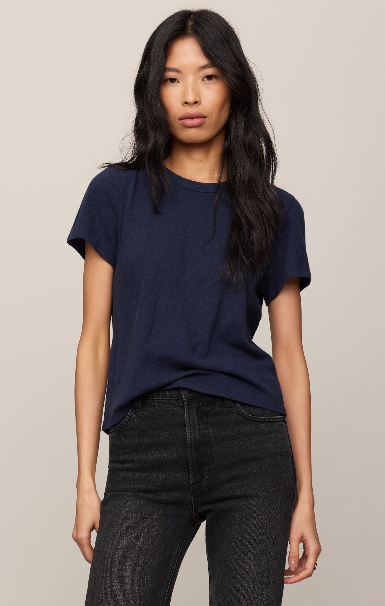 Woman wearing a navy blue t-shirt and black jeans against a beige background