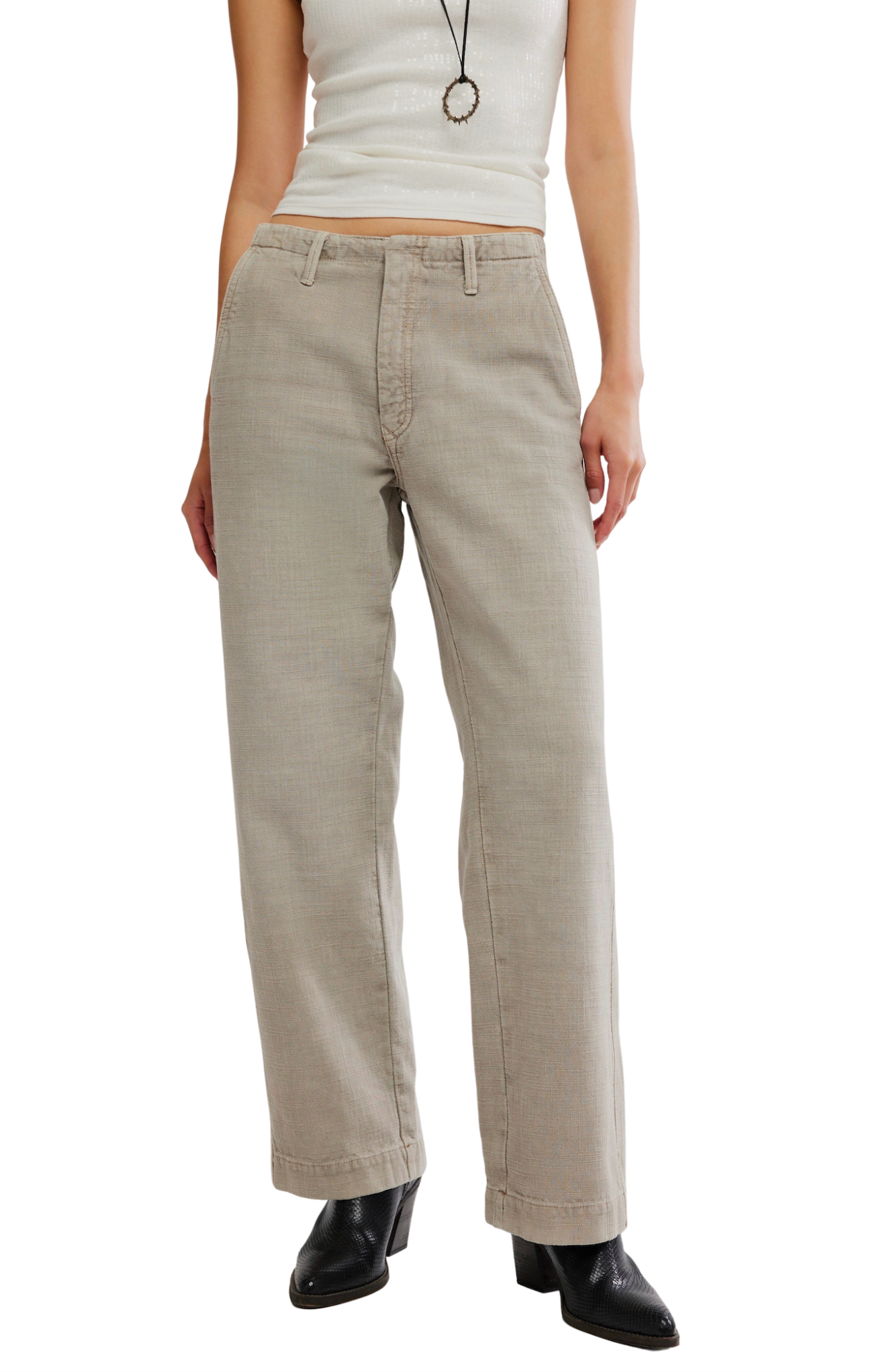 A model wearing straight-leg beige pants, a white sleeveless crop top, and black ankle boots, shown from the waist down against a plain white background.