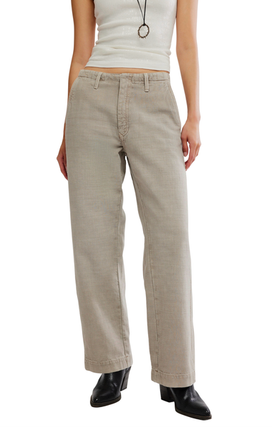 A model wearing straight-leg beige pants, a white sleeveless crop top, and black ankle boots, shown from the waist down against a plain white background.