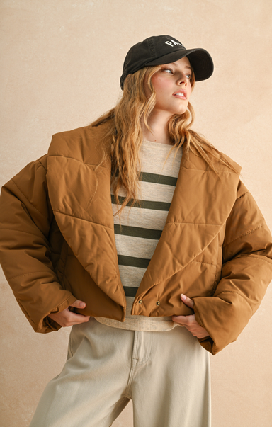 Person wearing a brown puffer jacket, striped shirt, and black cap against a beige background