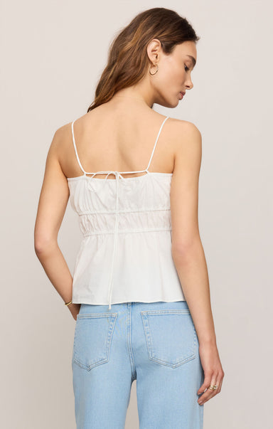 Woman wearing a white lace-up top and light blue jeans against a plain background