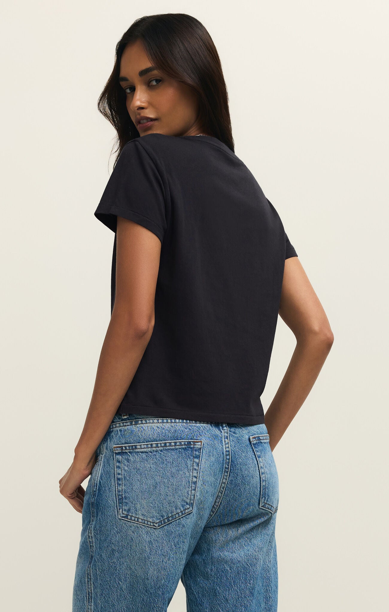 Woman wearing a black t-shirt and blue jeans on a plain background