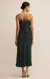 A woman wearing a dark green midi slip dress with lace trim and thin straps stands against a neutral background, paired with silver heels