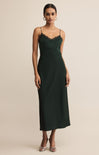 A woman wearing a dark green midi slip dress with lace trim and thin straps stands against a neutral background, paired with silver heels