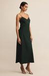 A woman wearing a dark green midi slip dress with lace trim and thin straps stands against a neutral background, paired with silver heels