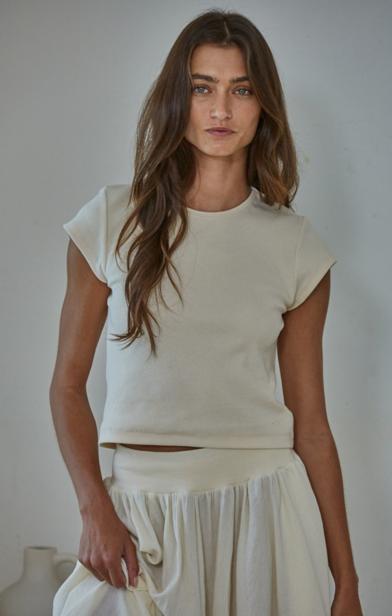 Woman wearing a white top and skirt against a plain background